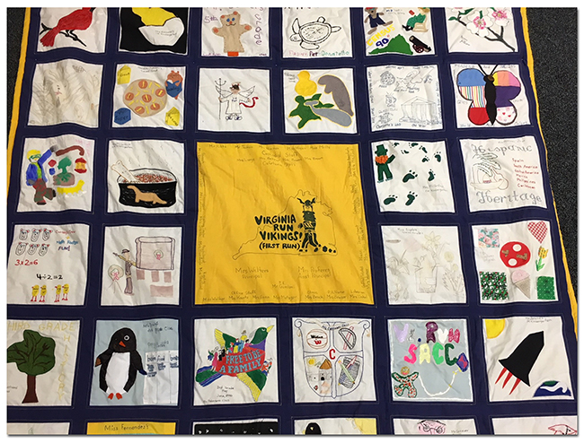 Photograph of a portion of the quilt. 27 squares are fully visible and include images of a cardinal, a bear puppet, a butterfly, a rocket, a penguin, a tree, a dinosaur, a leprechaun, dogwood blossoms, a turtle, a whale, and a manatee. The center panel, in yellow with blue lettering, is the image that appears on one of Virginia Run's first yearbooks, that of a cartoon Viking running across a map of the state of Virginia with the words: Virginia Run Vikings, First Run!
